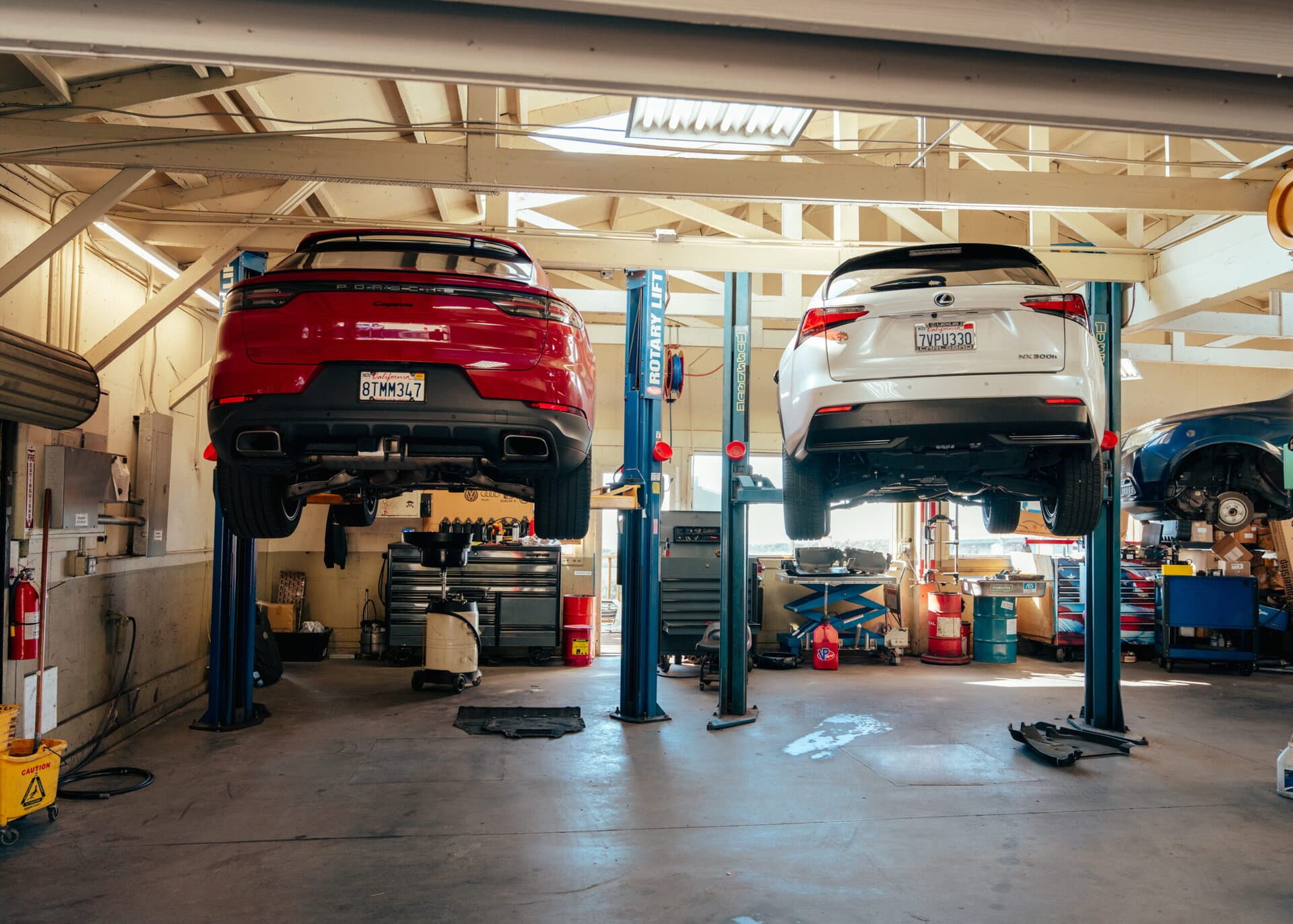 Two luxury SUVs lifted on hydraulic lifts inside a professional auto repair shop, showcasing vehicle maintenance and repair services at Del Mar Car Care.