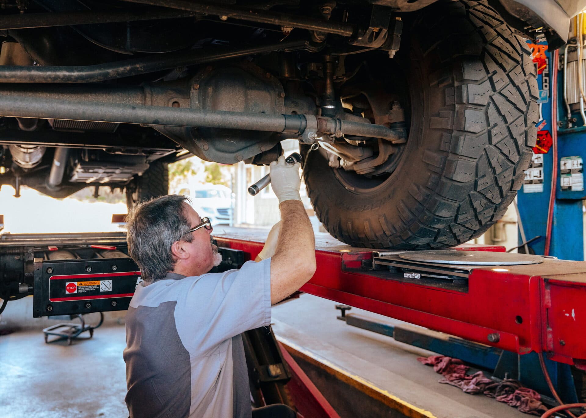 Auto mechanic inspecting vehicle undercarriage at Del Mar Car Care.