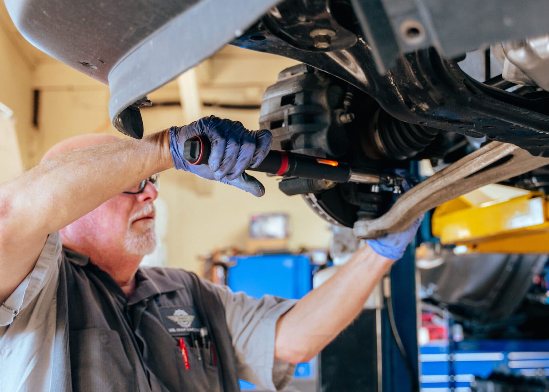 Auto repair technician inspecting under vehicle engine.