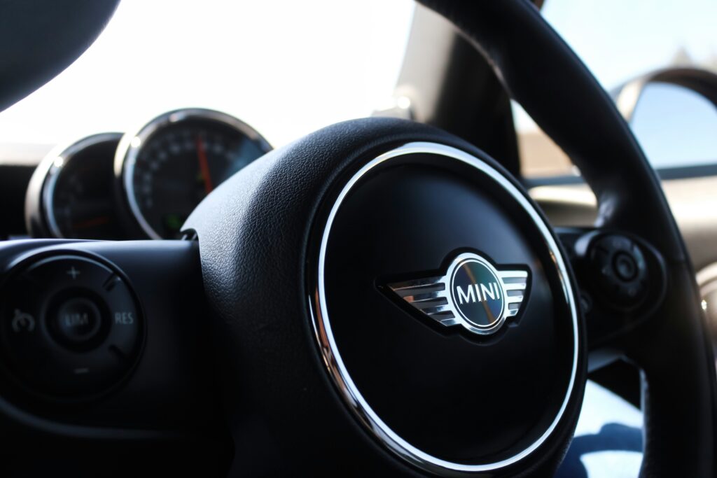Close-up of a Mini Cooper steering wheel with the iconic logo, highlighting the vehicle's stylish interior and premium craftsmanship. Perfect for car care and maintenance visuals.