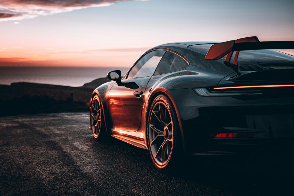 High-performance Porsche sports car parked by the coast during sunset, showcasing sleek design and luxury automotive craftsmanship.