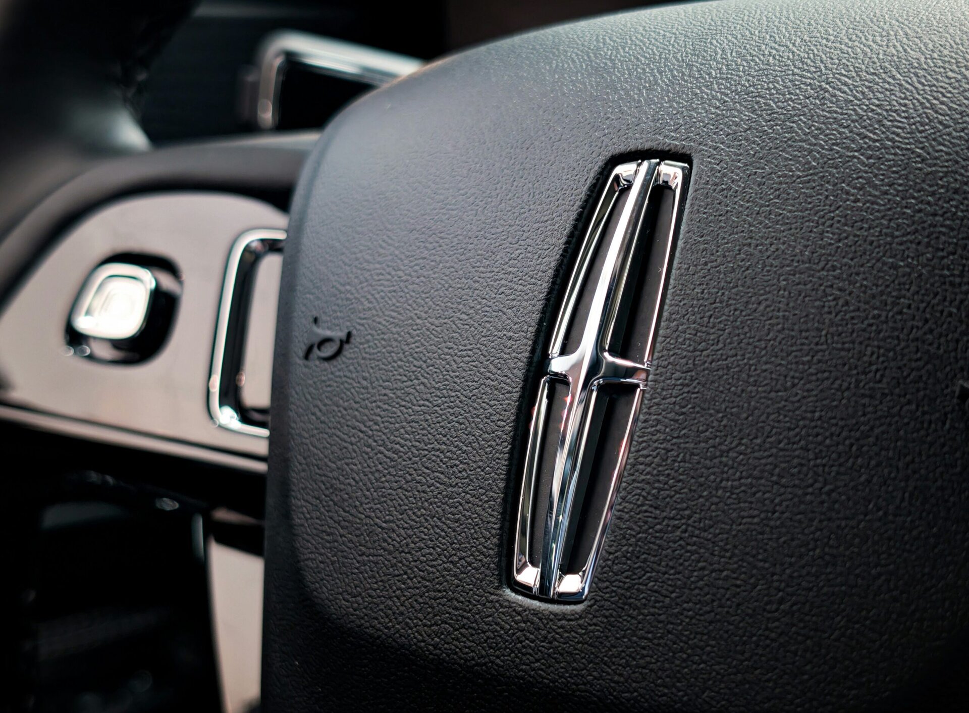 Close-up of a Lincoln logo on a car steering wheel, showcasing premium vehicle interior details.