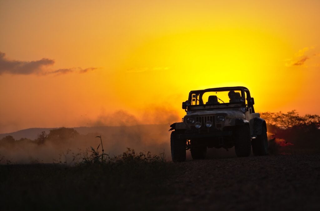 Jeep vehicle driving through dirt at sunset, showcasing off-road capabilities and outdoor adventure readiness.