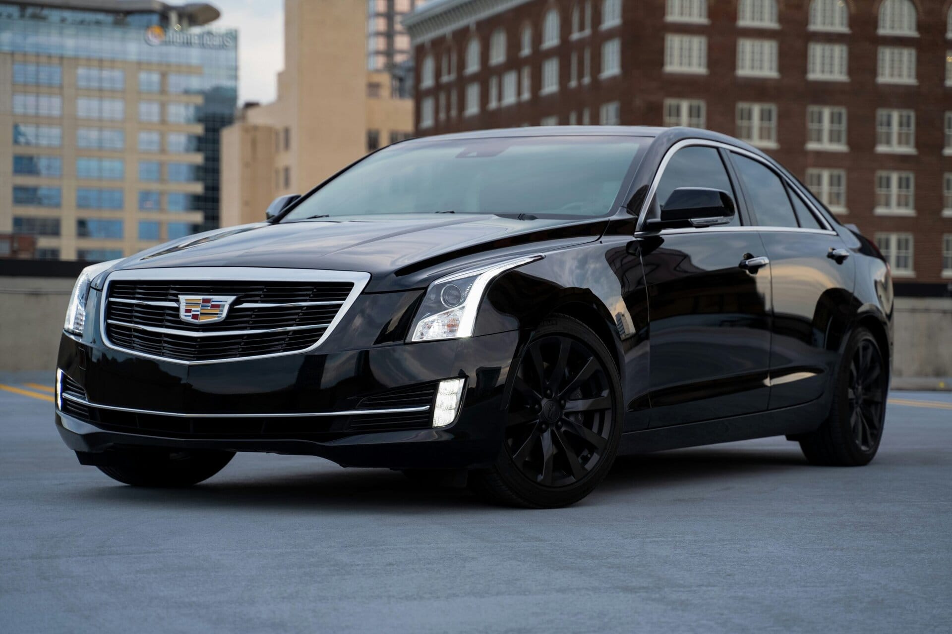 Black Cadillac sedan parked on city street with modern buildings in the background, showcasing luxury vehicle maintenance and detailing services at Del Mar Car Care.