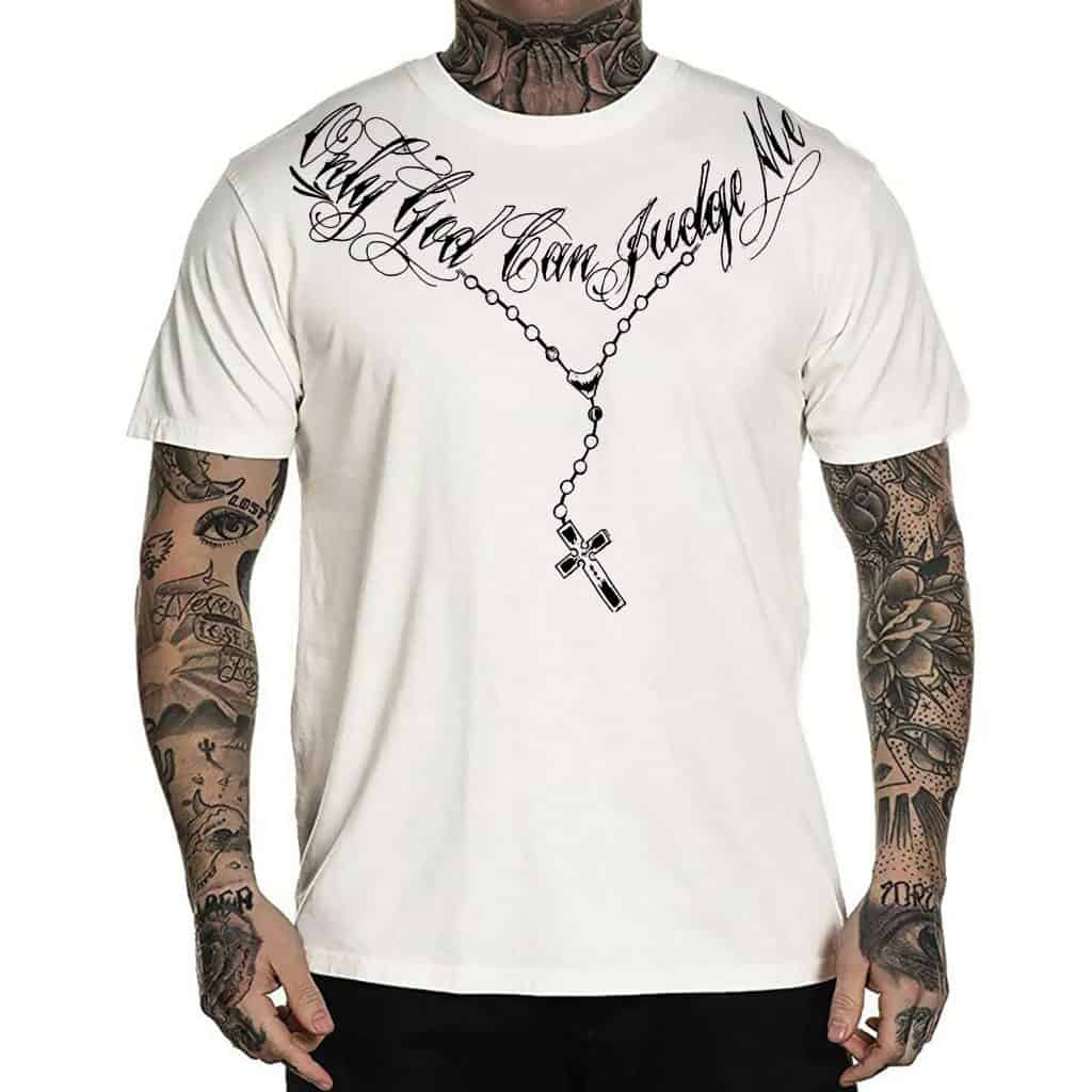 Rosary chain with bold scripted text "De Puta Madre" on a white streetwear t-shirt, featuring tattooed arms.