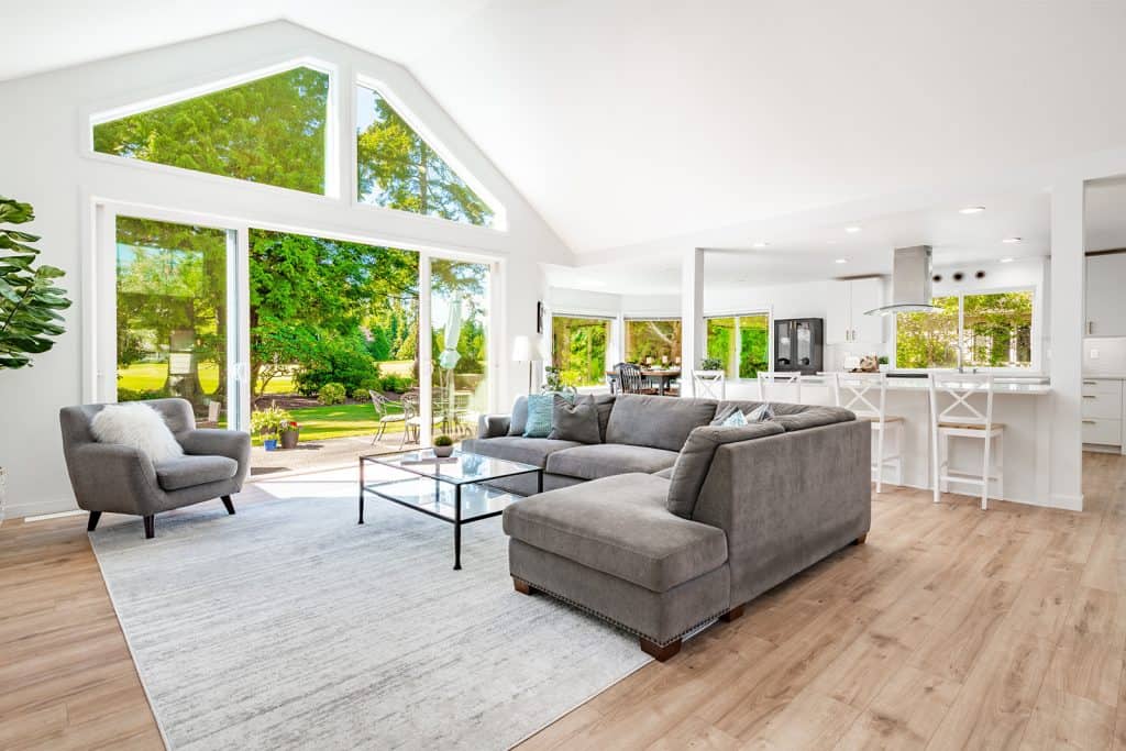 Bright living room and kitchen with windows, couch, chairs, stools, and counters.