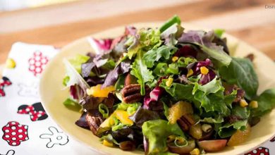 A colorful salad of greens, pecans, oranges, and corn on a yellow plate, served atop a Disney napkin for magical dining.