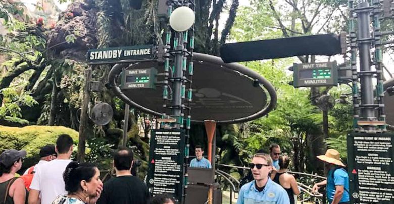 Guests line up for a theme park ride beneath digital displays showing the current standby entrance and estimated wait times.