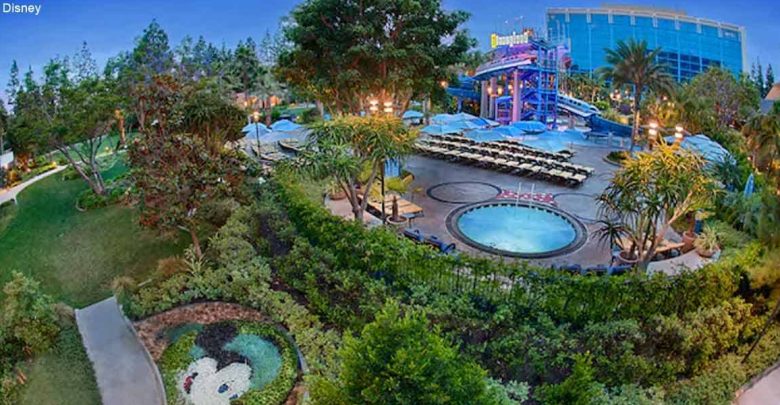 Aerial shot of Disneyland Hotel pool area featuring splashy water slides, lounges, and a Mickey-shaped garden for Disney fans.