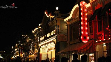 Main Street Arcade at Disneyland illuminated at night, glowing with vibrant signs as guests stroll through the lively atmosphere.