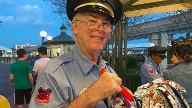 A cheerful security team member at the park entrance welcomes guests while holding a bright, colorful park souvenir.