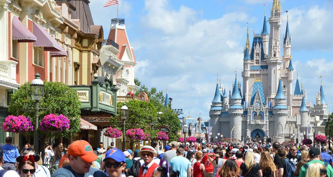 Guests stroll along Main Street, heading toward the iconic Cinderella Castle at Disney World under bright blue skies.