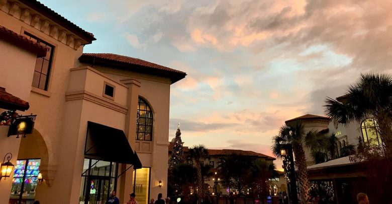 Guests wander along festively adorned Main Street at sunset, surrounded by twinkling lights and a vibrant sky.