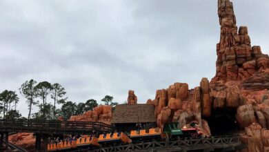 Big Thunder Mountain Railroad train races through dramatic red rocks and wild west scenery beneath a moody, cloud-filled sky.