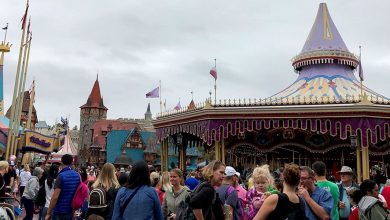 Visitors enjoy the lively atmosphere by the vibrant carousel at the amusement park, with clouds overhead setting the scene.