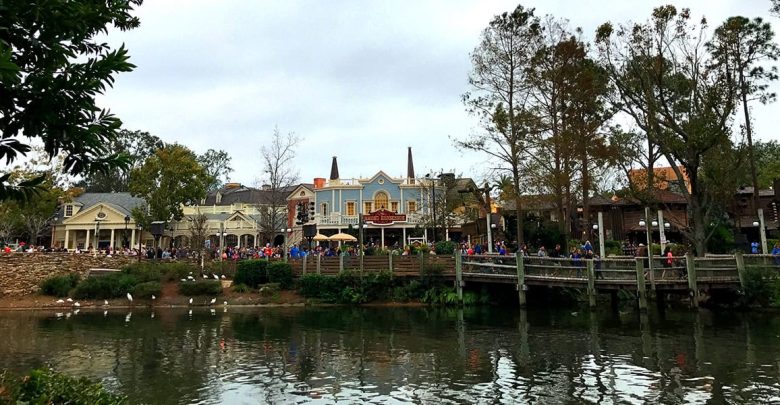 Guests stroll along a lively riverside boardwalk, lined with vibrant attractions and shops, all mirrored in the sparkling water.