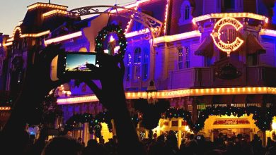 Guests at Universal Studios capture the illuminated Hogwarts Castle on their phones as evening falls, joined by a lively crowd.