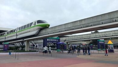 A green-striped monorail glides above guests at Walt Disney World’s bustling Transportation and Ticket Center.