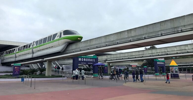 A green-striped monorail glides above guests at Walt Disney World’s bustling Transportation and Ticket Center.