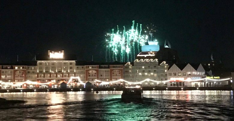 Green fireworks burst above waterfront buildings, reflecting on the water—just like Disney Enchantment outside Magic Kingdom.