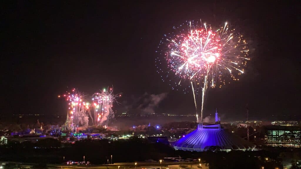 Disney Enchantment fireworks dazzle the night sky above a blue-lit building, illuminating the city just outside Magic Kingdom.