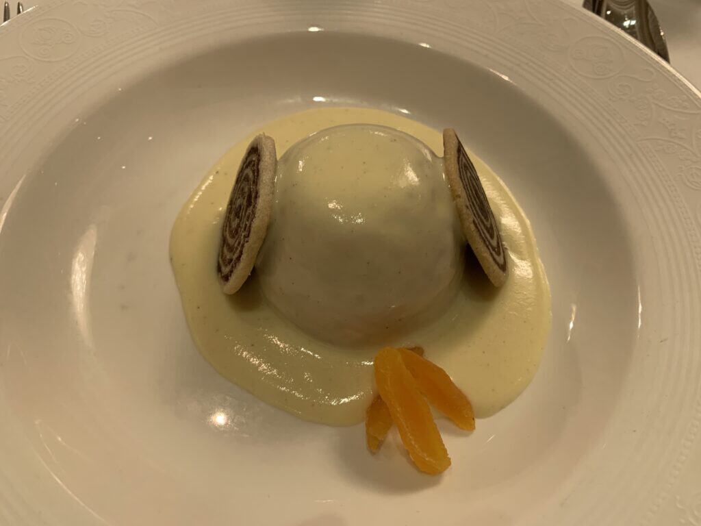 A Disney Fantasy-themed dome dessert with creamy sauce, two rolled cookies, and orange slices on a white plate.