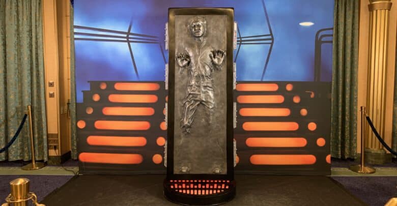 Han Solo frozen in carbonite greets guests with dramatic flair before Star Wars-themed red-lit steps and a futuristic backdrop.