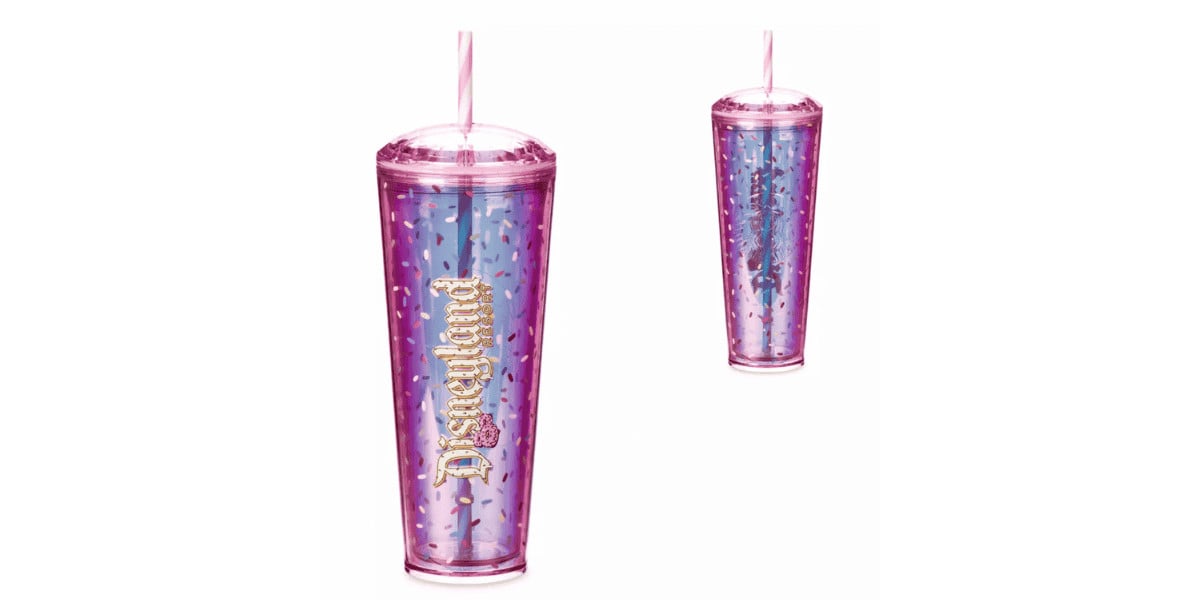 A tall, tapered tumbler with a lid and straw, featuring a holographic pink and blue design adorned with star patterns and the word "Disneyland" in gold script. Part of the Mickey Mouse Donut Collection, it has a double-walled design and is shown twice—one large and one smaller version.