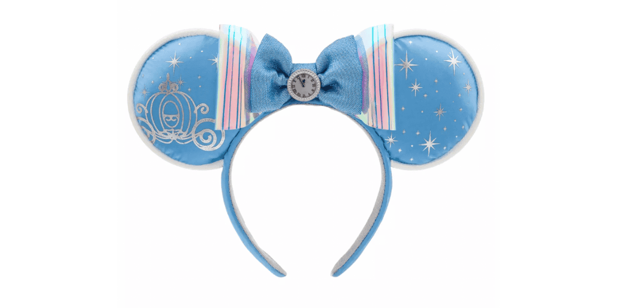 A blue headband with round, Tangled Mickey ears features a design of silver stars and a carriage on each ear. The center showcases a blue bow with pastel rainbow stripes and a decorative silver emblem with a clock face.