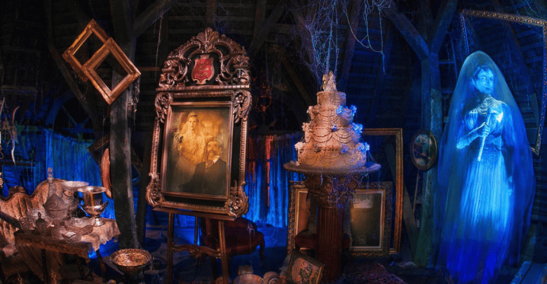 A dusty, dimly lit attic filled with antique items, including picture frames, a large ornate portrait, and an old cake from the Haunted Mansion Kitchen Collection. To the right, a ghostly blue figure of a woman in a long dress hovers, adding an eerie element to the scene. Cobwebs hang from the ceiling.