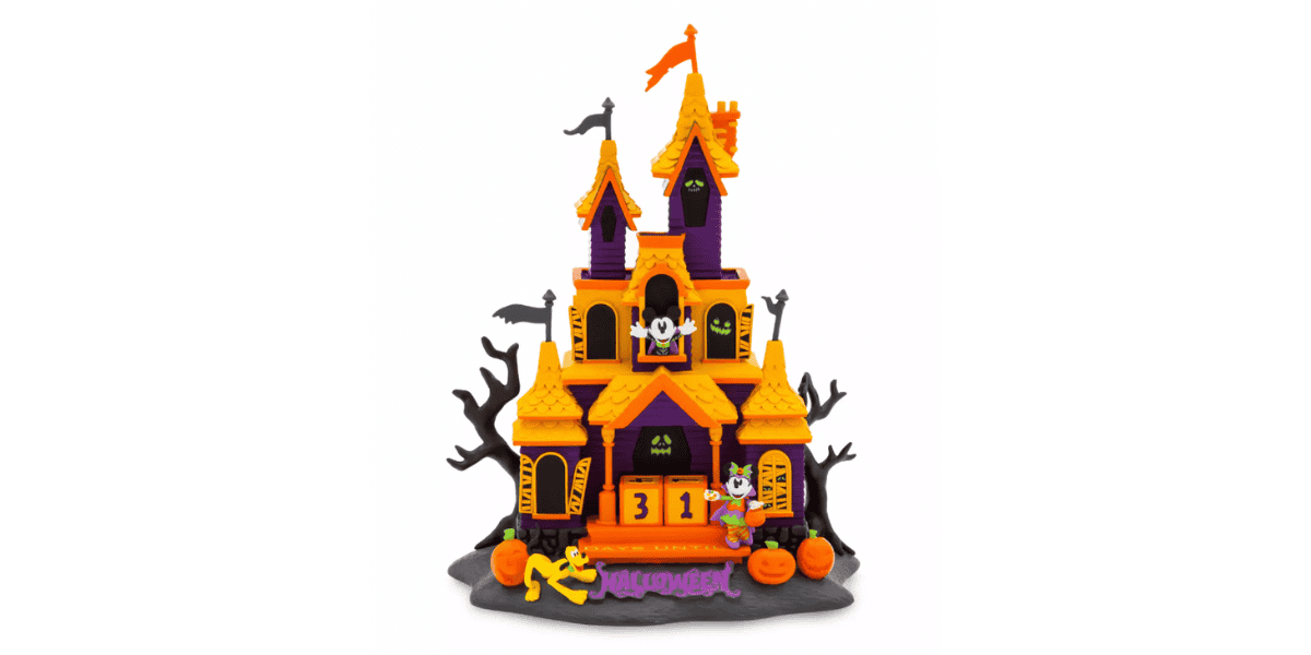 A colorful Halloween-themed haunted house display with orange and purple accents. The house has spooky decorations like bats, a ghost, and a skeleton. The front porch shows "31" for October 31st. Pumpkins and eerie trees surround the house, with "Halloween" written at the bottom.
