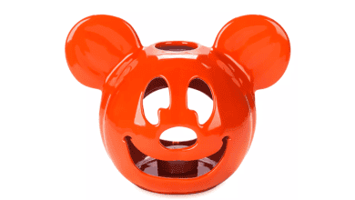 A bright orange ceramic candle holder shaped like the head of a cartoon mouse, with cutouts for the eyes, nose, and mouth. The design is playful and has two round ears protruding from the top.