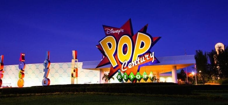 The entrance of Disney’s Pop Century Resort at night, featuring a brightly lit, colorful sign with bold letters and playful design elements against a deep blue sky.