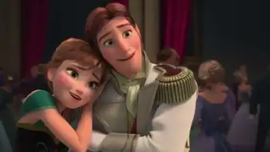 Animated characters Anna and Hans from Disney’s Frozen stand close together at a ball; Anna smiles and rests her head on Hans’s shoulder, while Hans smiles and holds her with his arms crossed. People dance in the background.