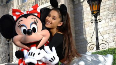 Ariana Grande wearing Minnie Mouse ears shares a joyful hug with Minnie Mouse in front of Cinderella Castle at Disney World.