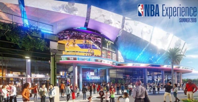 A vibrant exterior view of the nba experience attraction featuring a large crowd of visitors, illuminated signage, and screens showing basketball games.