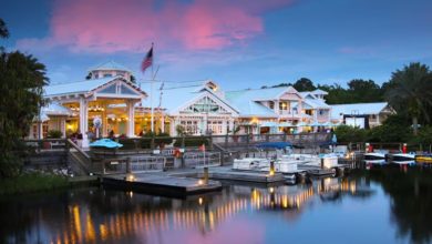 Lakeside hotel restaurant with boats, twinkling lights, and a pink Disney sunset reflected on the water—pure park enchantment.