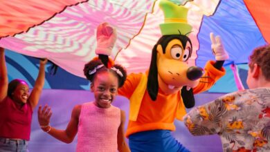 Goofy leads kids and an adult in parachute games at a lively indoor Walt Disney World celebration.