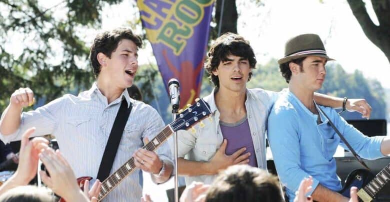The Jonas Brothers rock the outdoor stage, jamming on guitars and singing for excited fans beneath a Camp Rock Disney backdrop.