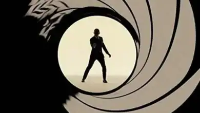 James Bond stands in sharp silhouette, dressed in his signature suit and aiming his gun directly at us, perfectly framed by the swirling gun barrel motif that signals his legendary arrivals—an iconic moment that brings the cinematic thrill of 007 to life for theme park guests seeking that unmistakable spy adventure energy.