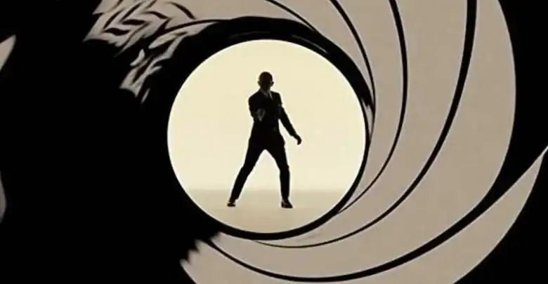 James Bond stands in sharp silhouette, dressed in his signature suit and aiming his gun directly at us, perfectly framed by the swirling gun barrel motif that signals his legendary arrivals—an iconic moment that brings the cinematic thrill of 007 to life for theme park guests seeking that unmistakable spy adventure energy.