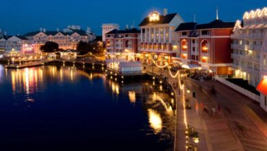 Disney World’s vibrant waterfront buildings and lively boardwalk glow with sparkling lights at night, their reflections shimmering across the peaceful water—creating a picture-perfect moment that captures the excitement and wonder of Disney just before the resort closes on August 10.