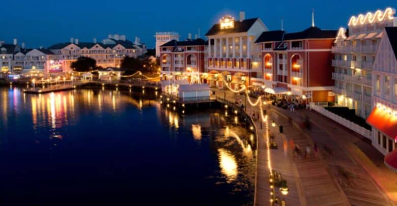 Disney World’s vibrant waterfront buildings and lively boardwalk glow with sparkling lights at night, their reflections shimmering across the peaceful water—creating a picture-perfect moment that captures the excitement and wonder of Disney just before the resort closes on August 10.