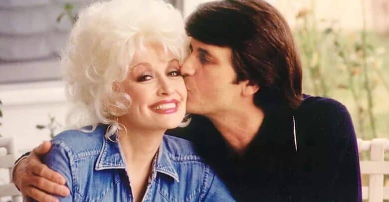 A couple shares a sweet moment at Dollywood, as a man kisses his smiling companion in her blonde hair and denim jacket, enjoying the lively atmosphere of the theme park’s outdoor setting.