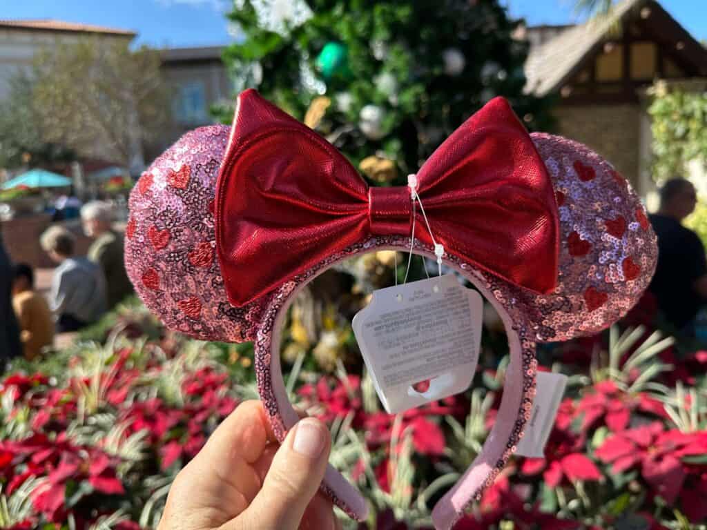 Colorful Disney Minnie Mouse ears headband with glitter pink sequins and a red bow, perfect for Disney theme park visits or holiday festivities.