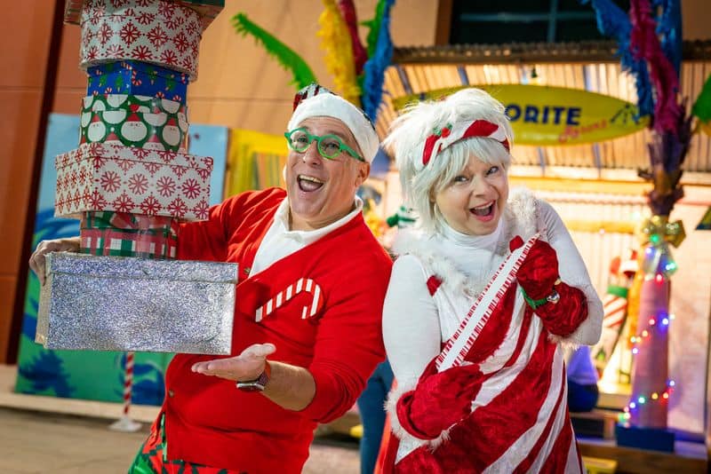 Cheerful Disney-themed Christmas costumes featuring Santa and Mrs. Claus with vibrant holiday decor in the background.
