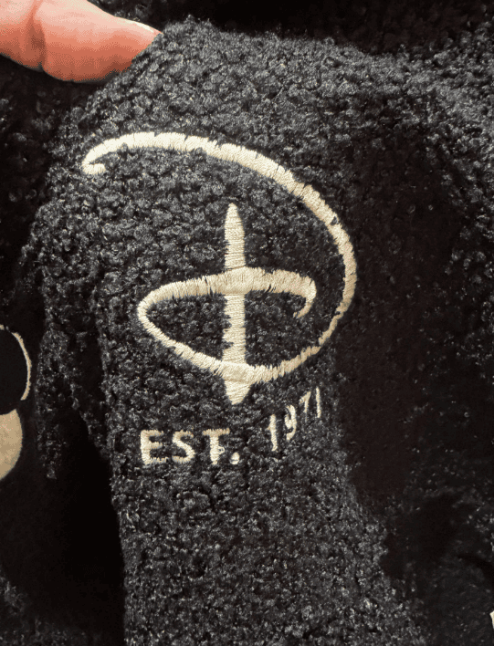 Close-up of black Disney hoodie with embroidered logo, textured fabric, and "EST. 71" text.