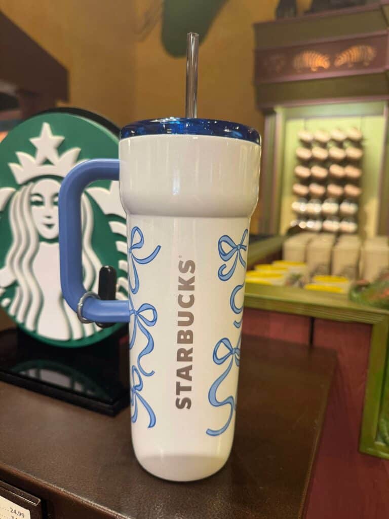 A white Starbucks tumbler with blue bows and a blue handle, featuring the Starbucks logo in the background.