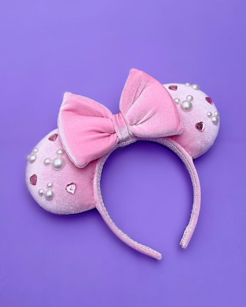 Cute pink Minnie Mouse headband with bow, pearls, and heart accents, perfect Disney fashion accessory.