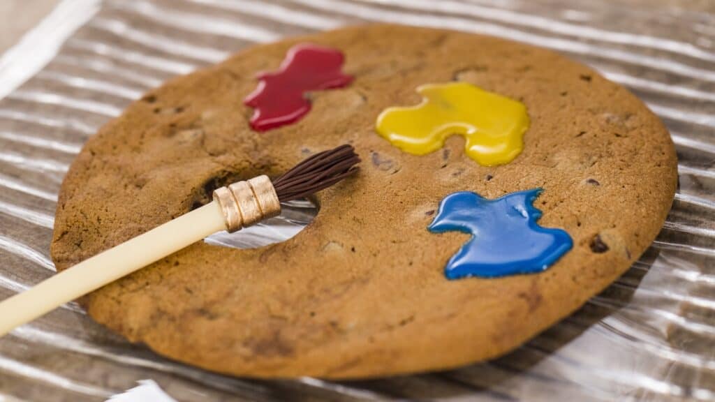 Edible cookie decorated with vibrant red, yellow, blue icing, and a paintbrush for Disney themed art.